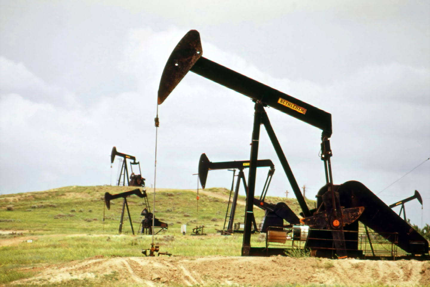 Oil pumpjacks in a grassy field under a cloudy sky.