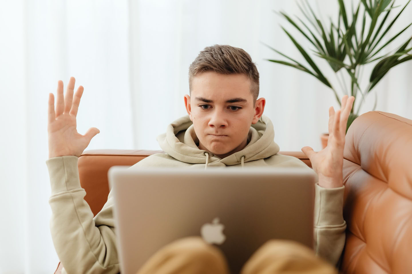 A teenager sitting on a couch with a laptop on their lap, looking mad