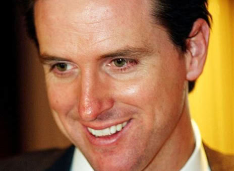 A man in a suit and tie smiling, with a blurred background.